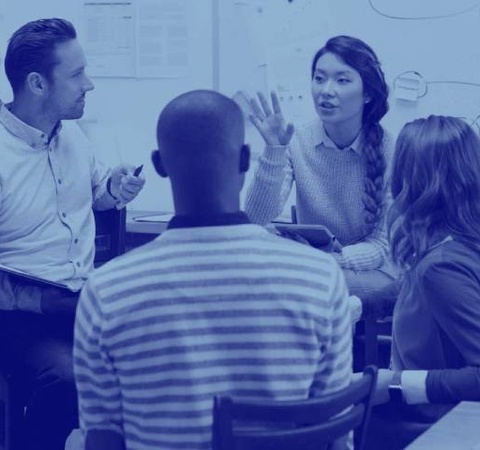A group of four people, two women and two men, are engaged in a discussion in an office environment.