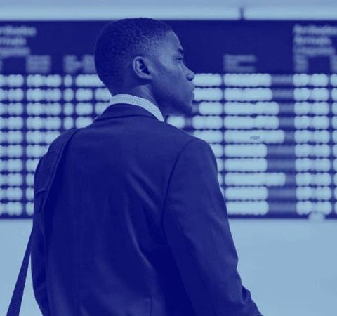 A businessman in a suit standing at an airport looking at the flight information monitor.