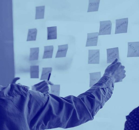 Two people are standing in front of a whiteboard, interacting with sticky notes.