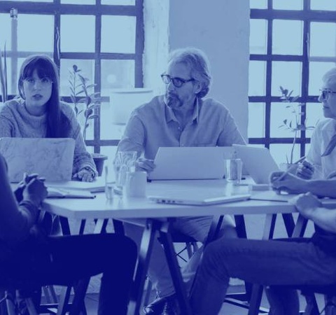 A group of professionals sitting around a table in a meeting room discussing over laptops