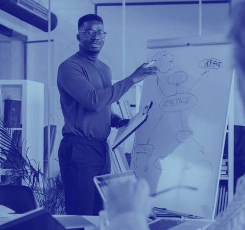 A man presenting a business strategy on a whiteboard to colleagues in an office setting.
