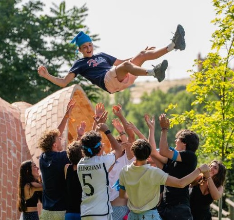 A young man performs a flip being tossed by a group of friends in a park