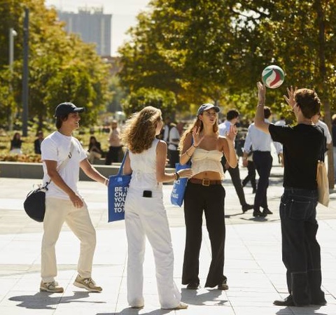 Group of people casually playing with a soccer ball in a sunny urban square.