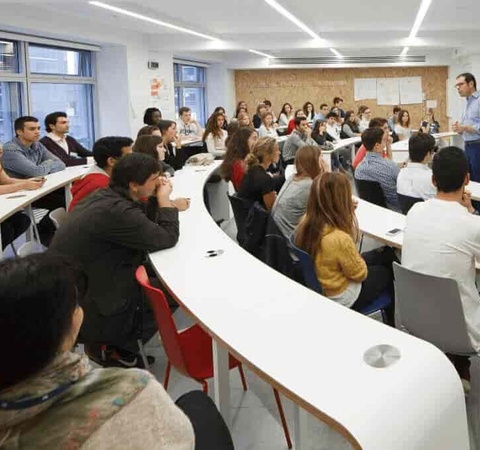 A man is speaking to a group of attentive adult students in a modern classroom setting.