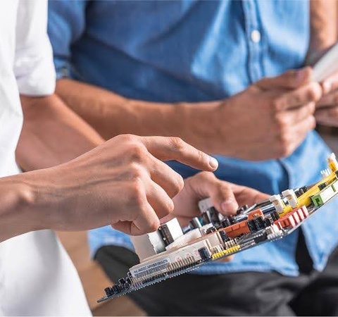 Two individuals are examining a circuit board with various components.