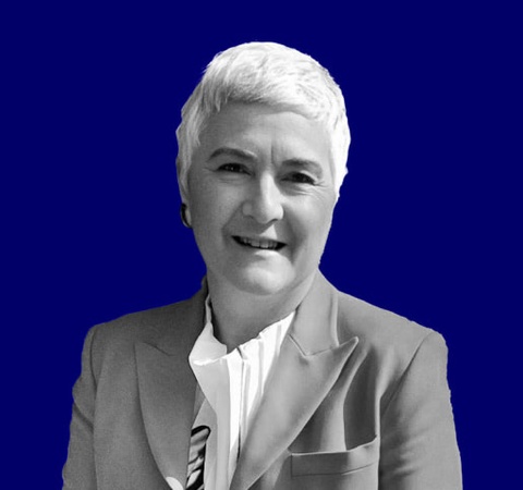 A monochrome image of a smiling woman with short hair, dressed in a suit, against a blue background.