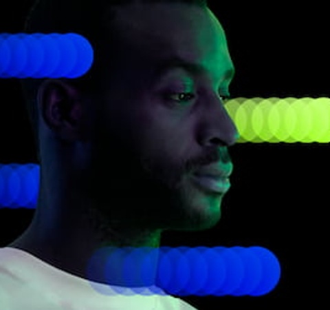 A man is looking at a tablet with colored light bars above in a dark setting.