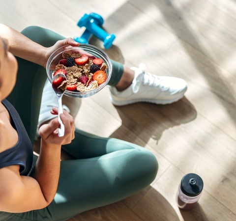 A person enjoying a healthy bowl of mixed fruits and granola after a workout.