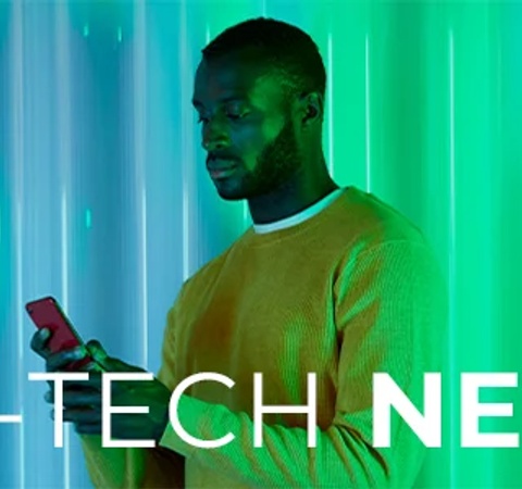 A man in a yellow sweater is using a smartphone against a futuristic green-lit background with the text 'SCI-TECH NEWS'.