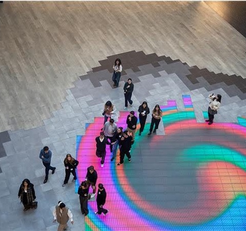 A vibrant digital art installation on the floor with people gathered around it.