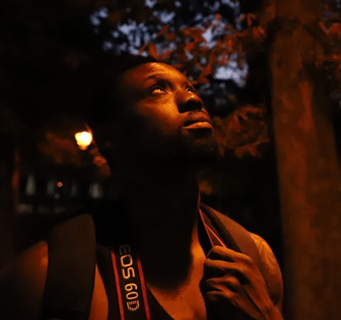 A man looks up thoughtfully in a dimly lit park at night
