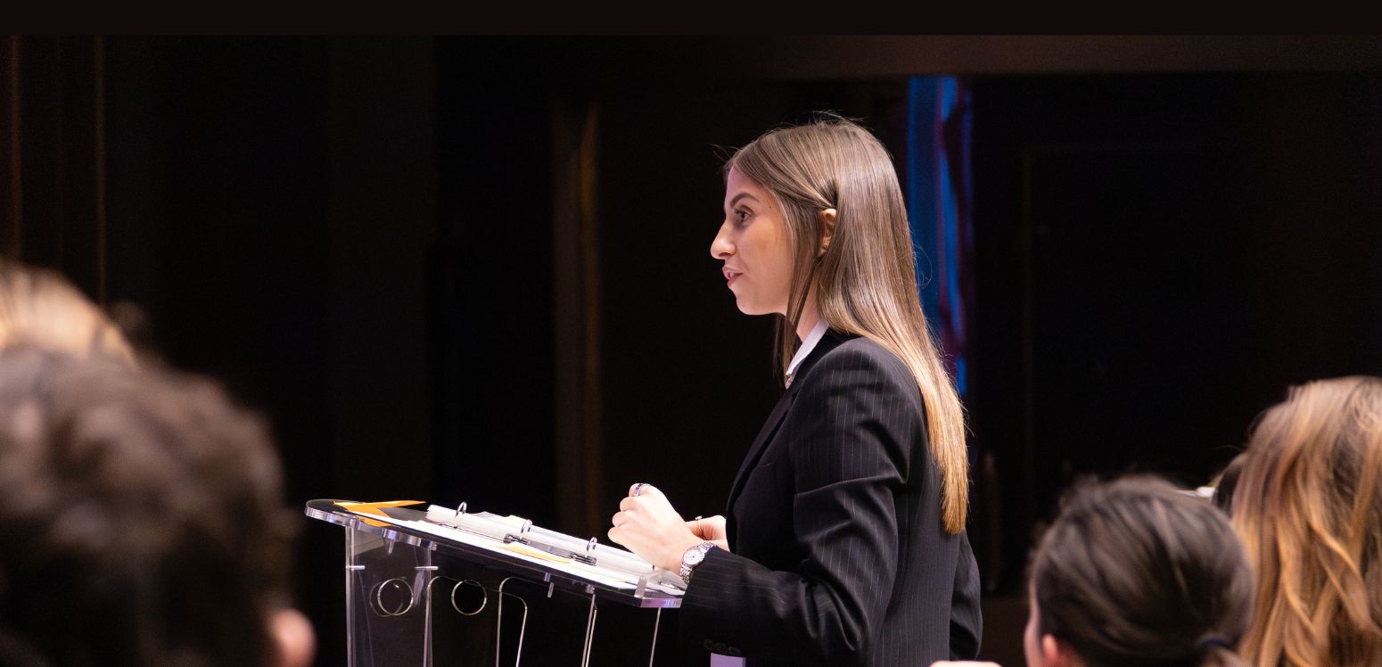 A young woman is delivering a speech at a podium in front of an audience.