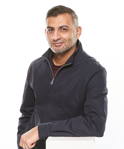 A man in a dark zip-up jacket smiling at the camera against a white background.