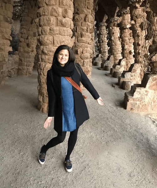 A woman smiling and posing between tall stone columns in an ancient, historical site.