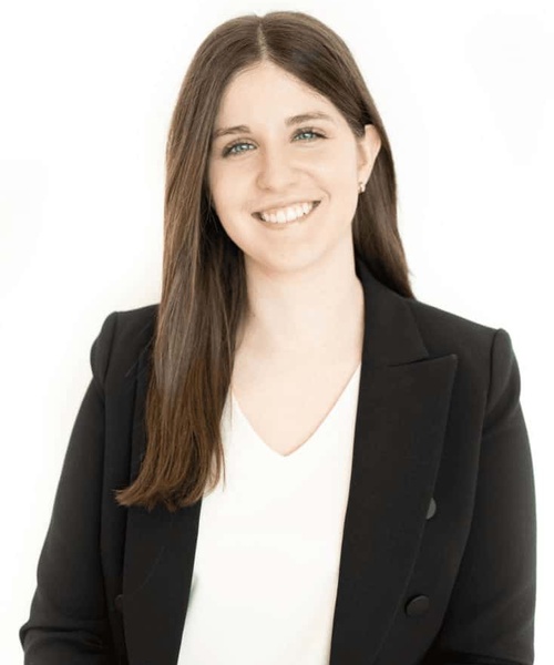 A professional portrait of a smiling woman wearing a black blazer over a white top against a white background.