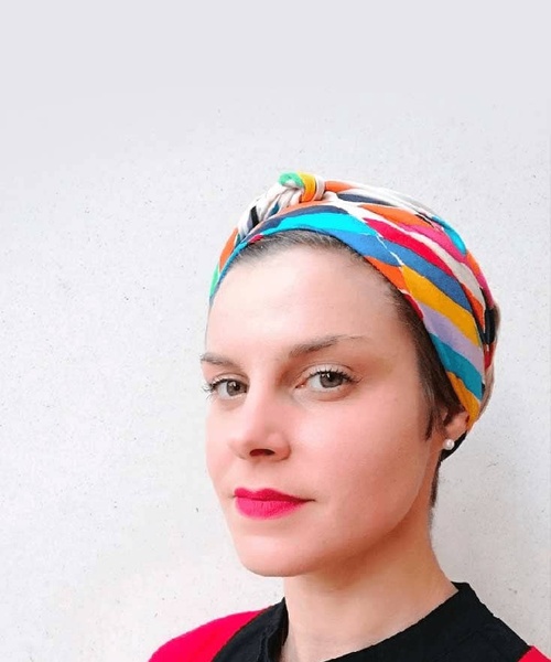 A woman with a colorful headscarf and red lipstick poses against a plain background.