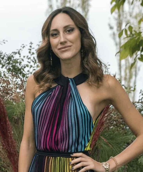 A woman in a colorful striped dress standing in a garden.