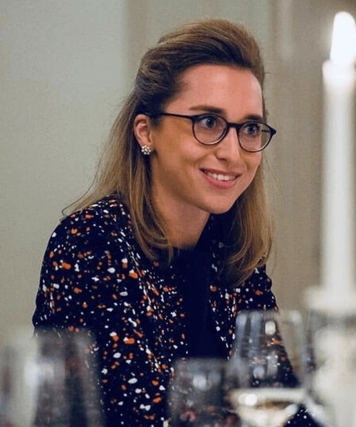 A smiling woman with glasses wearing a patterned dress at a dinner setting.