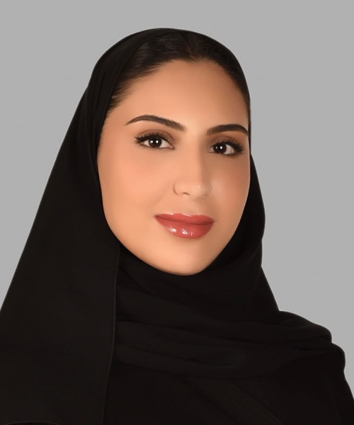 Portrait of a smiling woman wearing a black hijab against a gray background.