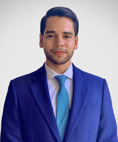 A professional portrait of a young man in a blue suit with a turquoise tie.