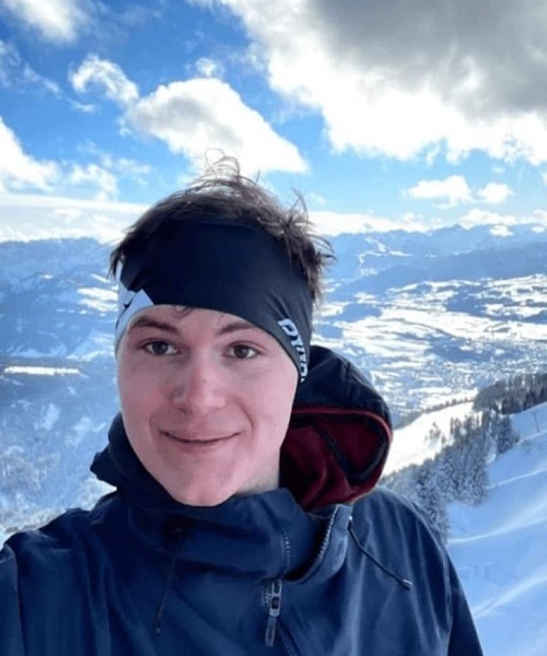 A person smiling at the camera with a snowy mountain landscape in the background.
