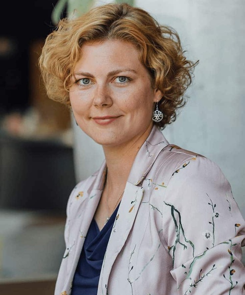 A portrait of a woman with short curly hair, wearing a floral blazer and a dark top, looking at the camera.