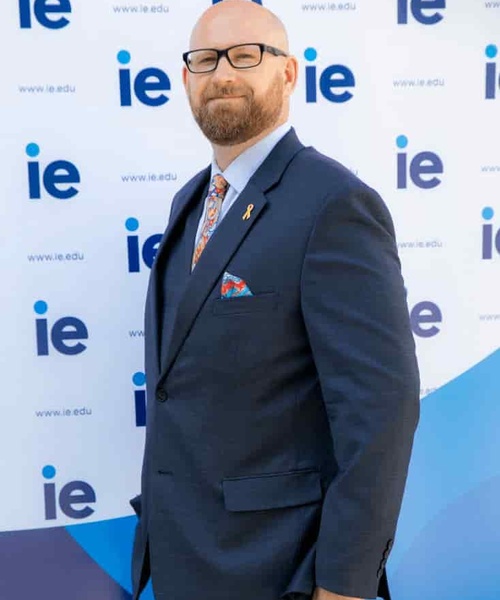 A man in a suit stands in front of a backdrop displaying the 'ie.edu' logo.