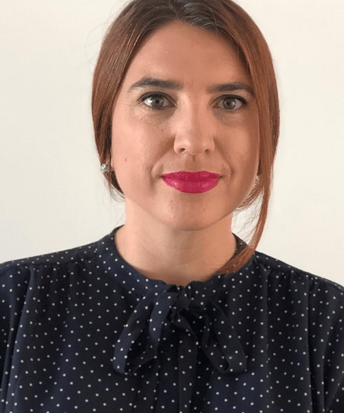 A woman with pink lipstick wearing a navy blue polka dot blouse.