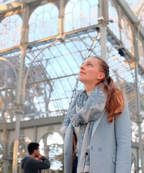 A woman admiring the architecture of a large glass structure, with a man in the background.