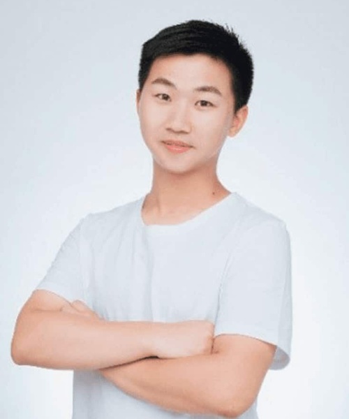 A young Asian man in a white t-shirt, standing with his arms crossed, smiling gently against a light gray background.