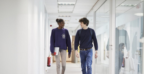 Two young people are walking together in a modern hallway.