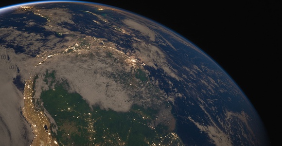 A view of Earth from space showing part of a continent illuminated by city lights under a dusky sky.