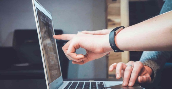 A person pointing at a laptop screen while another person watches.