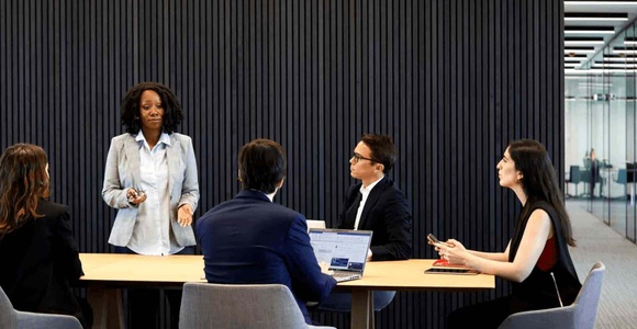 A business meeting with five professionals around a table in a modern office setting.