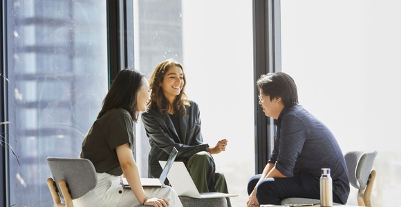 Three colleagues are engaged in a conversation in a bright, modern office space.