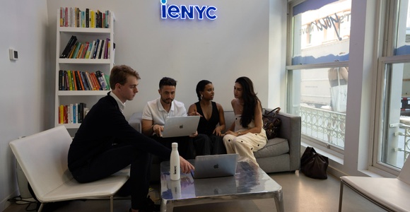 A group of four people engaged in a discussion while working on laptops in a modern office space.