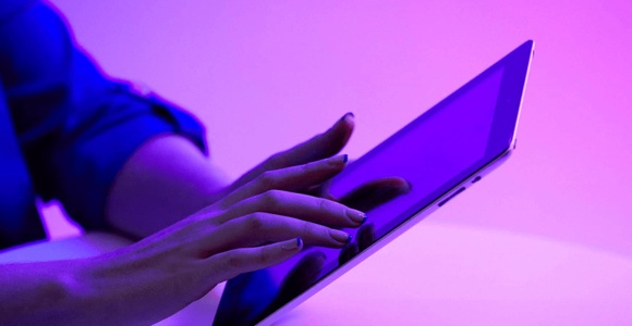 A person using a laptop in a room illuminated by purple light.