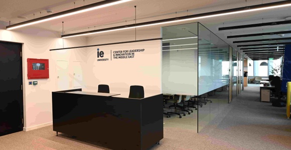 A modern office reception area with a sleek black desk and a glass-walled meeting room.