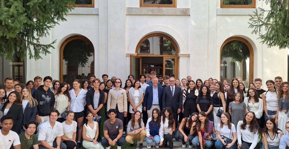 A large group of students posing for a photo with a few adults in front of a building with a classic facade and green lawn.