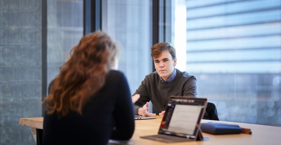 A young man is engaged in a conversation with a woman in a modern office setting.