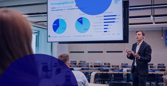 A speaker presents demographic data in a classroom setting with a large screen displaying charts.