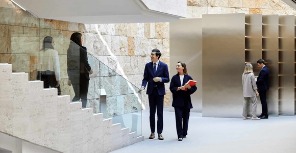People in a modern corporate building interior, featuring a sleek design with marble and minimalist elements.