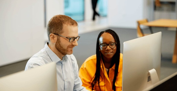 A man and a woman working together on computers in a modern office setting.