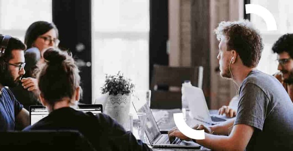 A group of people working together in a modern office environment with laptops and headphones.