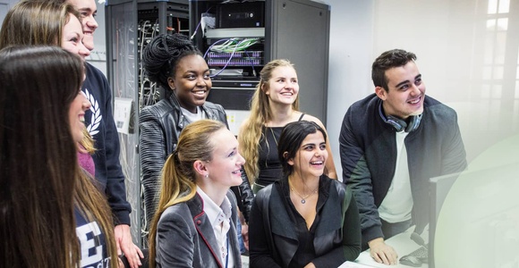 A group of people gathered around a computer, looking engaged and smiling.
