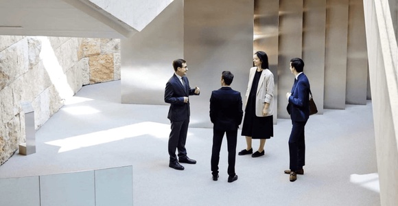 Four business professionals standing and conversing in a modern architectural setting with large columns and natural light.