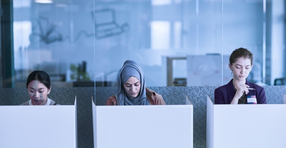 Three women are working quietly in a modern office space with cubicles.