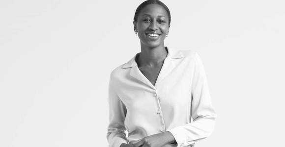 A black and white image of a smiling woman in a white blouse and light trousers.