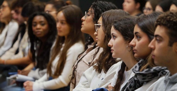 A group of young people is attentively sitting in a seminar or lecture hall.