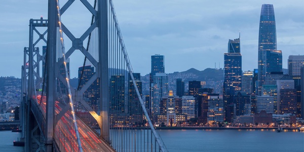 A scenic view of a city skyline with a bridge in the foreground at dusk.